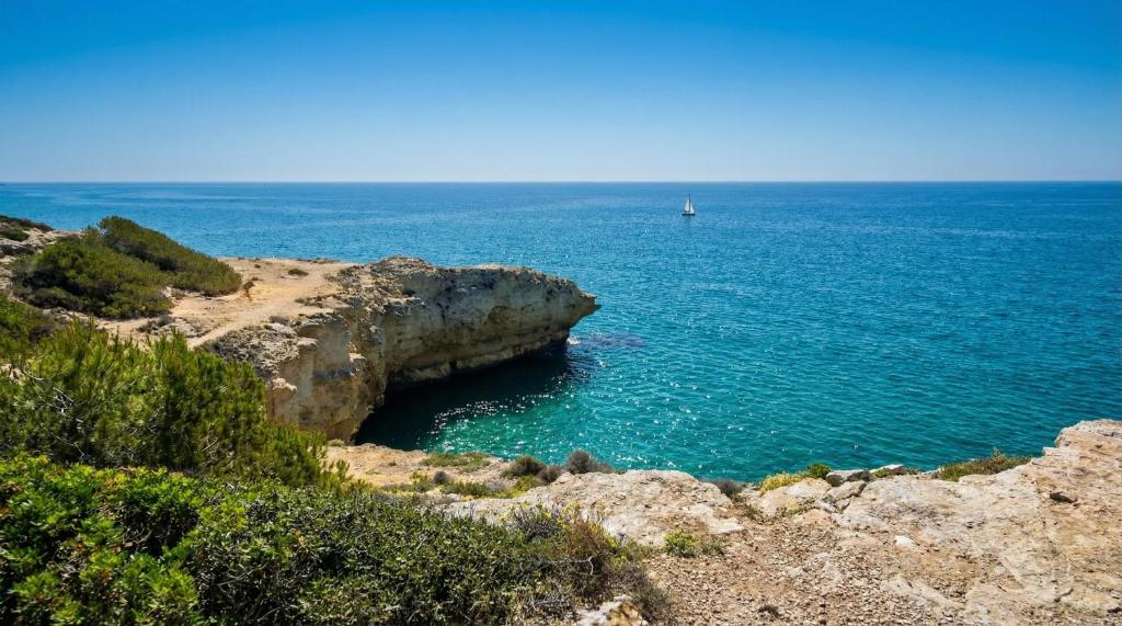 a boat in the ocean next to a cliff at Villa Playa del Sur A 250 metros de una magnifica playa Capacidad más de 16 AC 6 Suites Piscina XL in Torredembarra