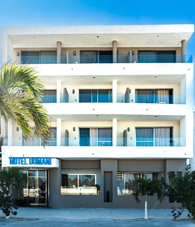 a white building with a palm tree in front of it at Hotel & Suites Domani in Progreso