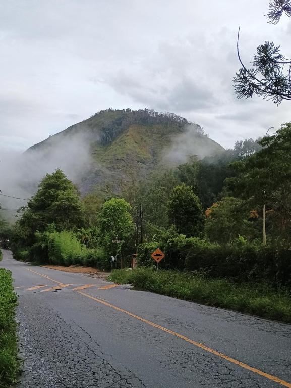 a road with a mountain in the distance with clouds at Hospedagem do Rio in Nova Friburgo