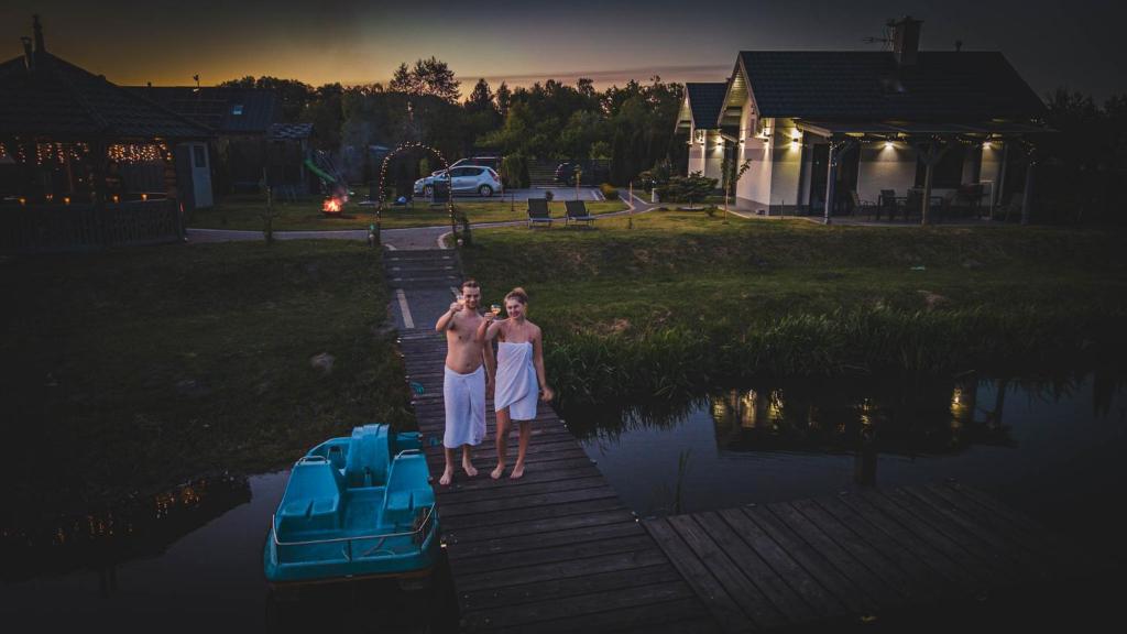 two people standing on a dock next to a boat at Hygge Domki in Junoszyno