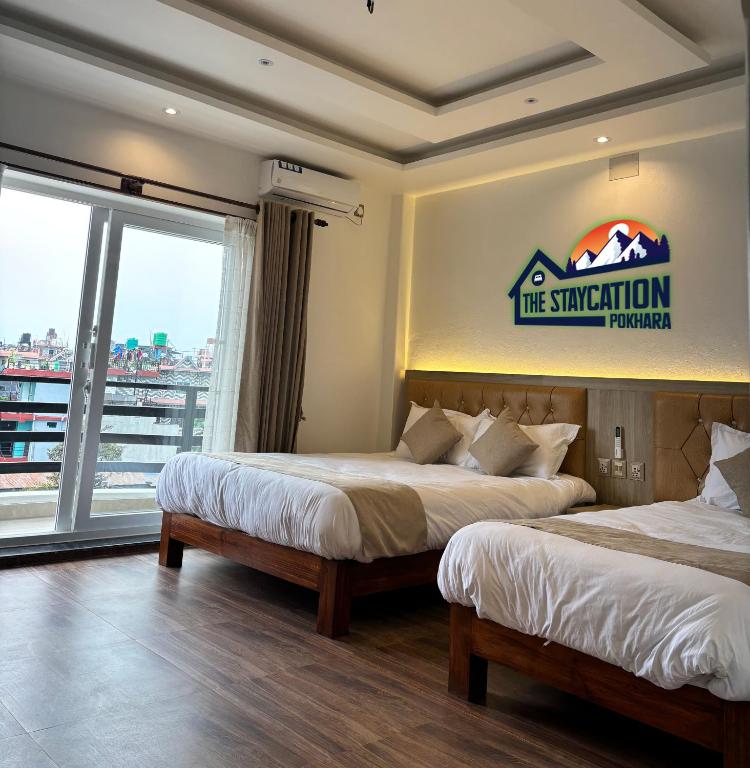 two beds in a room with a sign on the wall at The Staycation Pokhara in Pokhara
