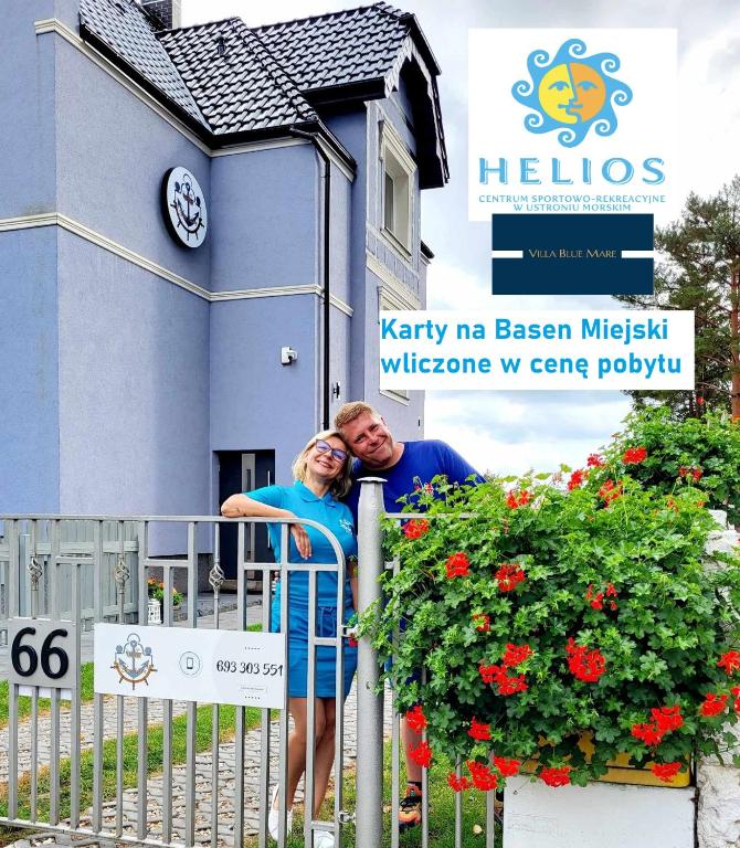 a man and woman leaning on a fence in front of a building at Villa Blue Mare I Gastro Wałówka Ciepłe napoje w cenie pobytu in Ustronie Morskie
