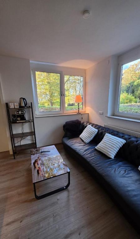 a living room with a black leather couch and two windows at Moderne 3-Zimmer-Wohnung mit separatem Eingang in Donauwörth