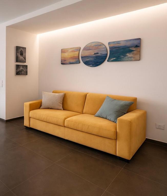 a yellow couch in a living room with three paintings at Appartamento Leon in Roseto degli Abruzzi
