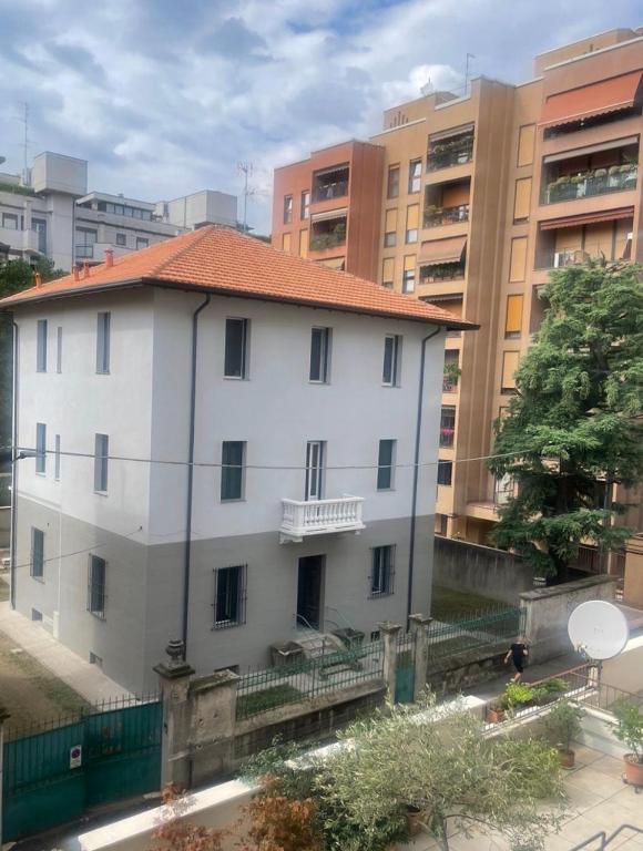 a white building with a red roof in a city at Lacasabianca guest house saronno in Saronno