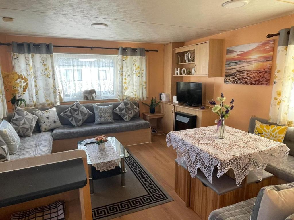 a living room with a couch and a table at Bright Family Caravan with Deck & BBQ at Seawick Holiday Park, Clacton in Clacton-on-Sea