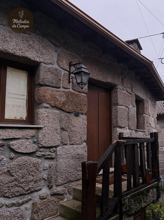 a stone house with a wooden door and a porch at Melodia do Campo in Terras de Bouro