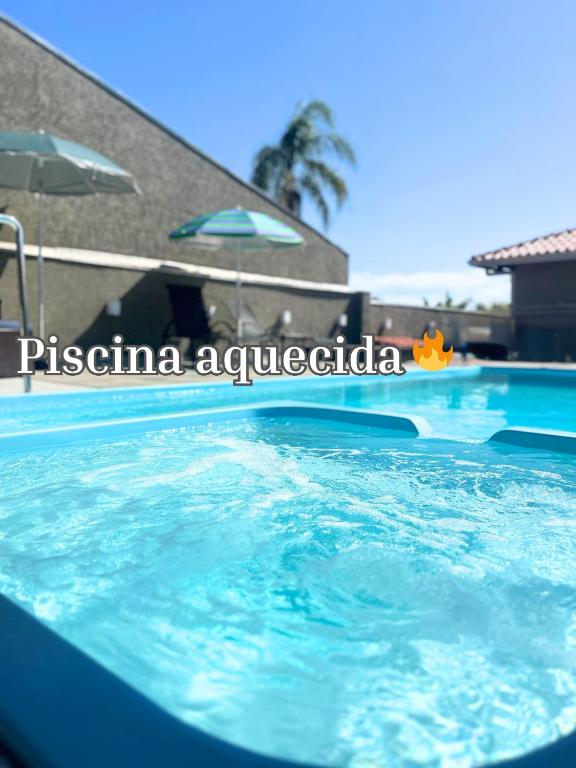 a swimming pool with blue water and an umbrella at Casa Sol da Manhã - Piscina aquecida com hidromassagem - 300m da praia in Guaratuba