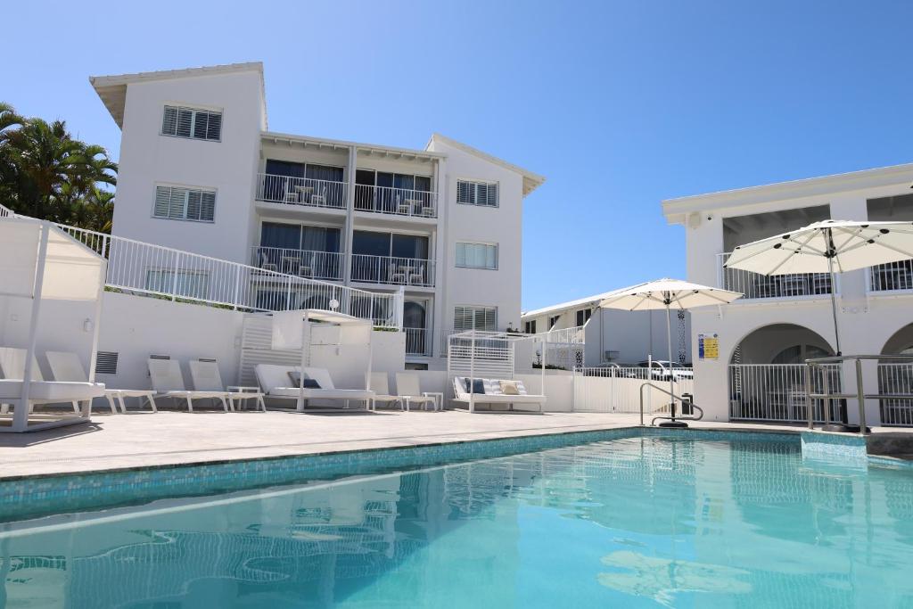a pool with chairs and umbrellas next to a building at Don Pancho Beach Resort in Bargara