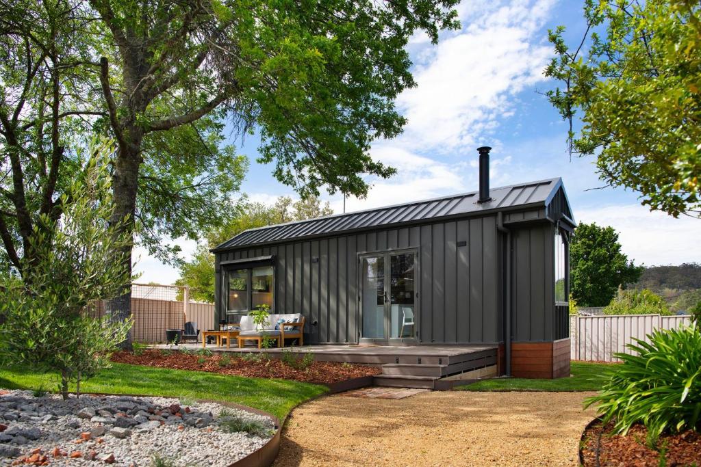 ein kleines schwarzes Haus in einem Garten mit Terrasse in der Unterkunft Piccola Blu Tiny House in Hepburn