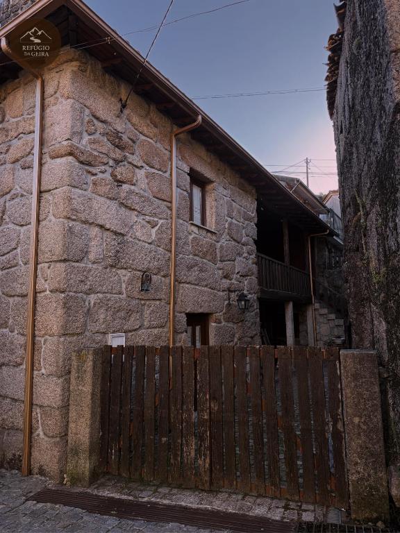 a stone house with a wooden fence in front of it at Refúgio da Geira in Campo do Gerês