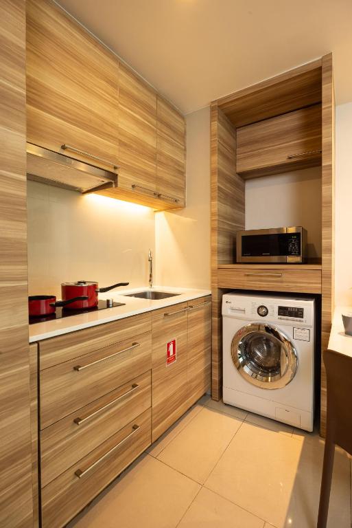 A compact wood-finished kitchenette with an induction hob, sink, microwave, and front-loading washer-dryer.