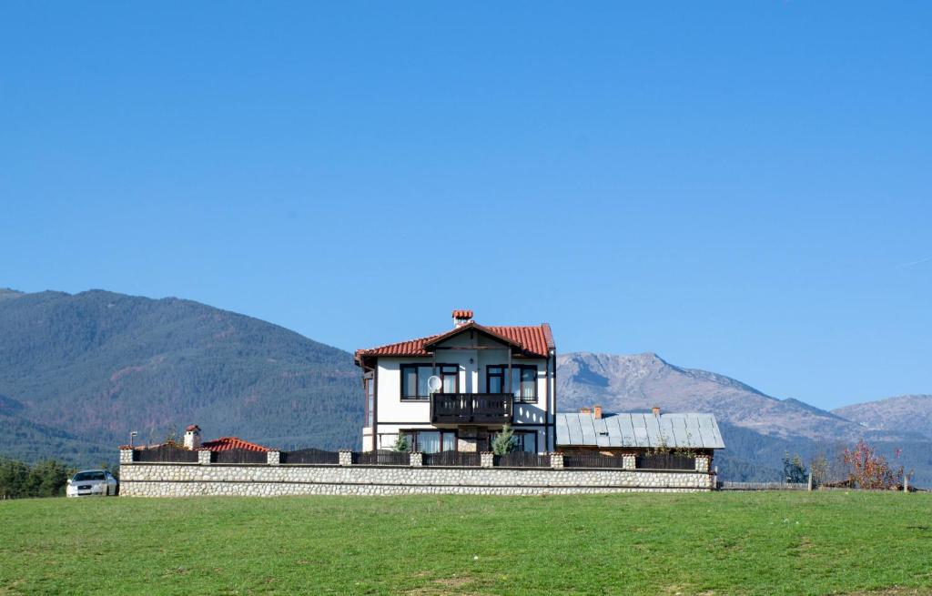 ein Haus auf einem Feld mit Bergen im Hintergrund in der Unterkunft Guest House Tommy Bansko - Bachevo in Bachevo