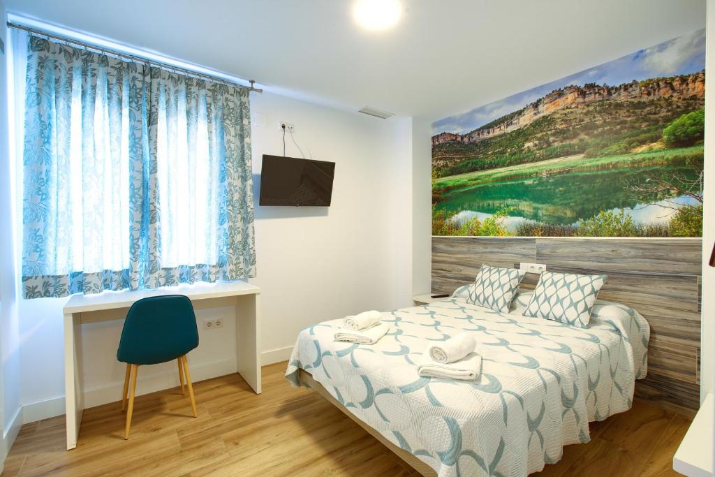 a bedroom with a bed and a desk and a painting at New Hostal Cabañas in Carboneras de Guadazaón