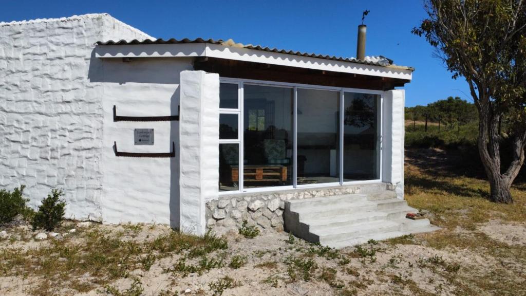 a small white building with a window on a field at Lumberjack Cottage at Blombosch Game Farm in Yzerfontein