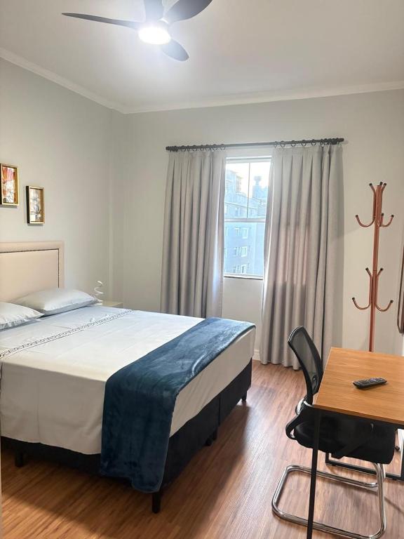 a bedroom with a bed and a table and a window at Dias Felizes - Apto Centro Serra Negra - Edifício Cisne in Serra Negra