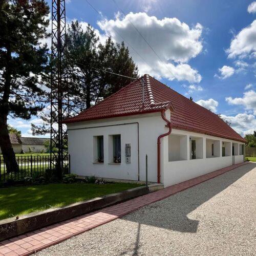 a small white building with a red roof at Fenyőudvar Vendégház Mocsa in Mocsa