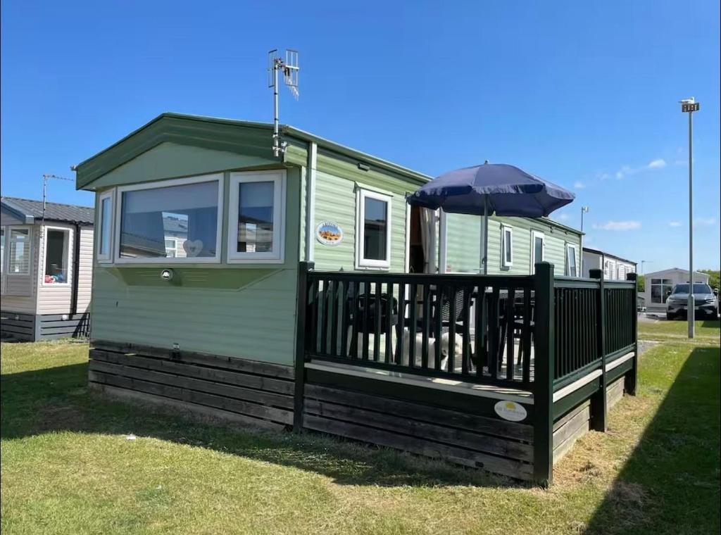 a green tiny house with an umbrella on the deck at Seaside Arizona in Morecambe
