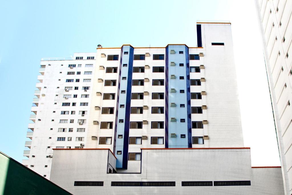 a tall white apartment building with blue windows at Apart Hotel Bhally INN in Balneário Camboriú