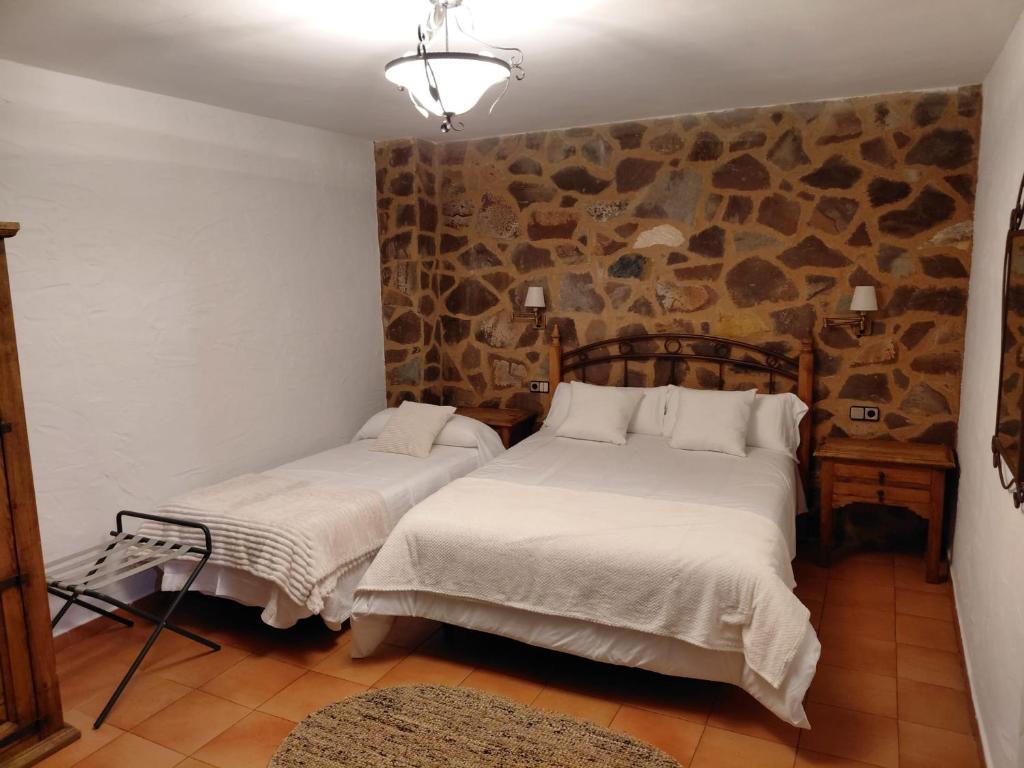 two beds in a room with a stone wall at Hotel Rural La Posada de Lía in Berzocana