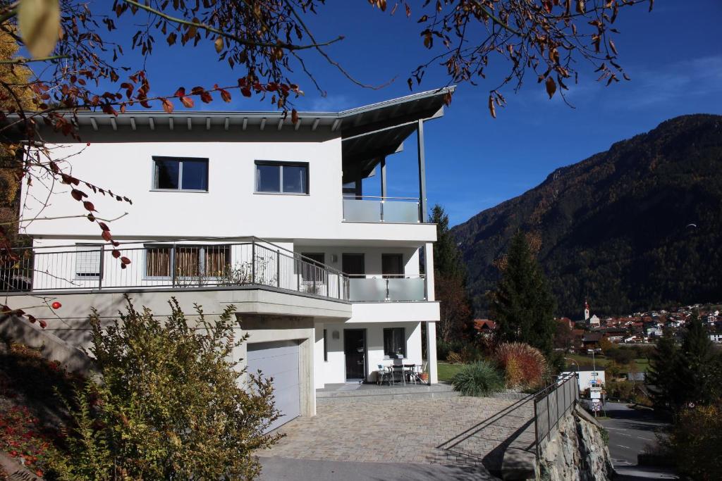 a white house with a balcony and mountains in the background at Appart Collina in Pfunds