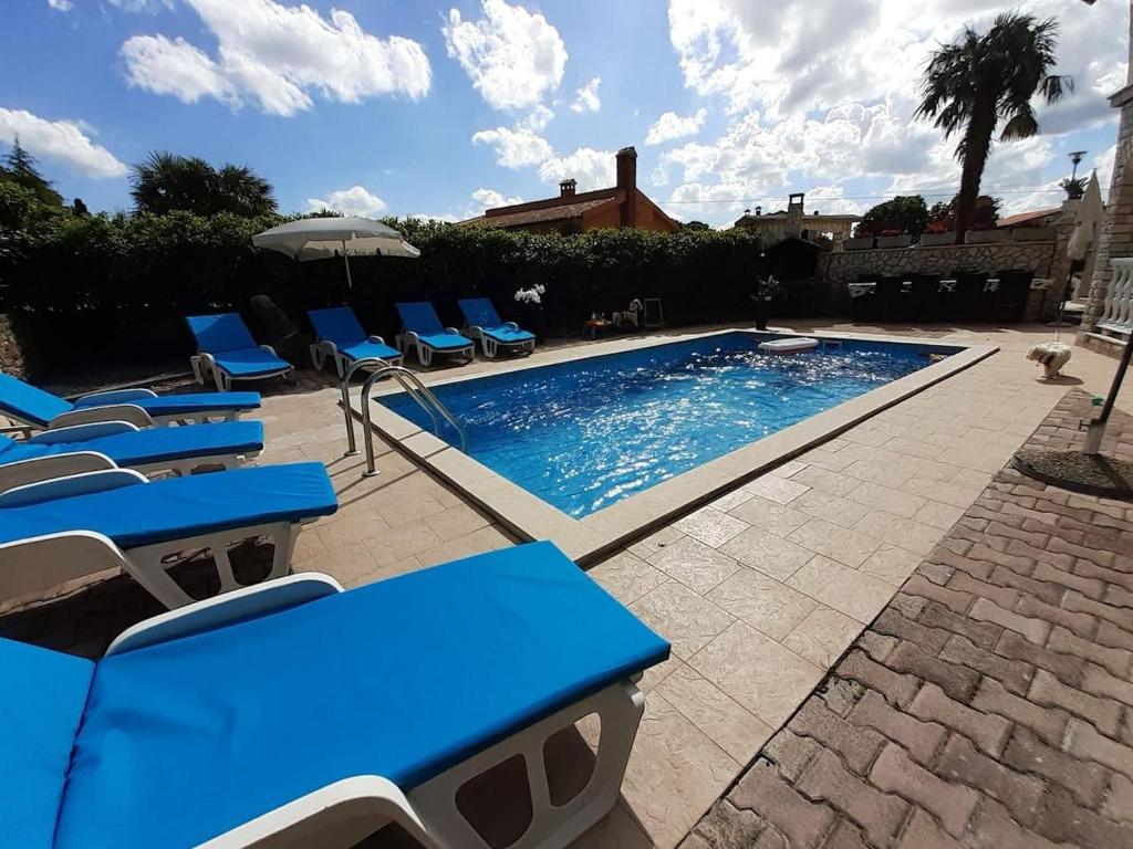 a swimming pool with blue chairs and an umbrella at Family-friendly apartments with swimming pool Nedescina, Central Istria - Sredisnja Istra - 7455 in Nedeščina