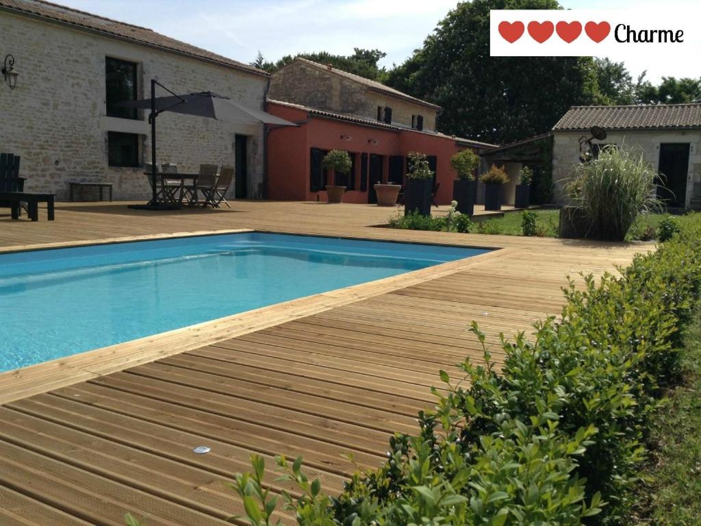 a swimming pool with a wooden deck next to a house at La Grange d'Aunis in Aigrefeuille-dʼAunis