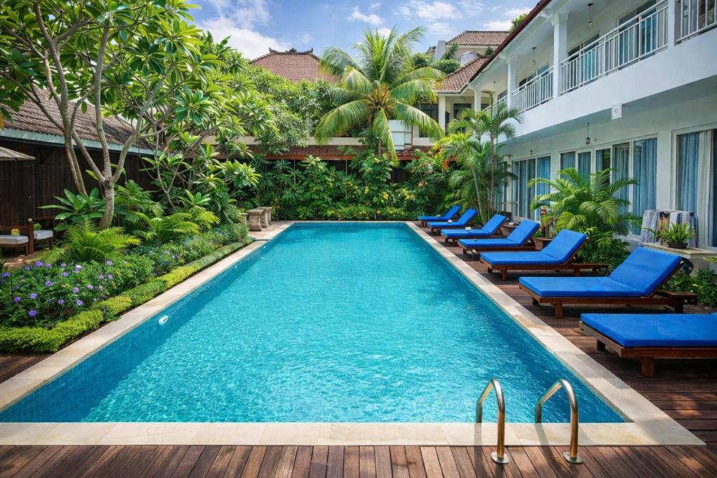a pool at a hotel with blue chairs and trees at Easy Surf Camp in Kuta