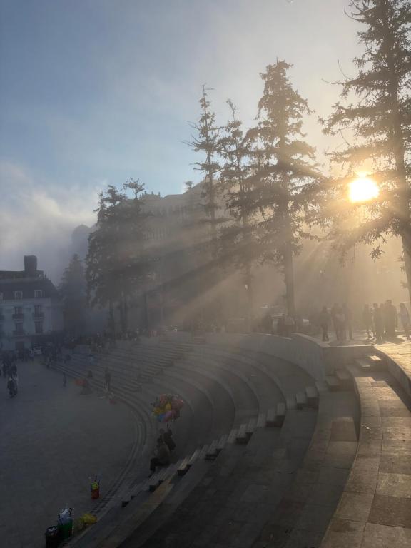 a foggy street with the sun rising behind trees at OnTop Hotel in Sapa