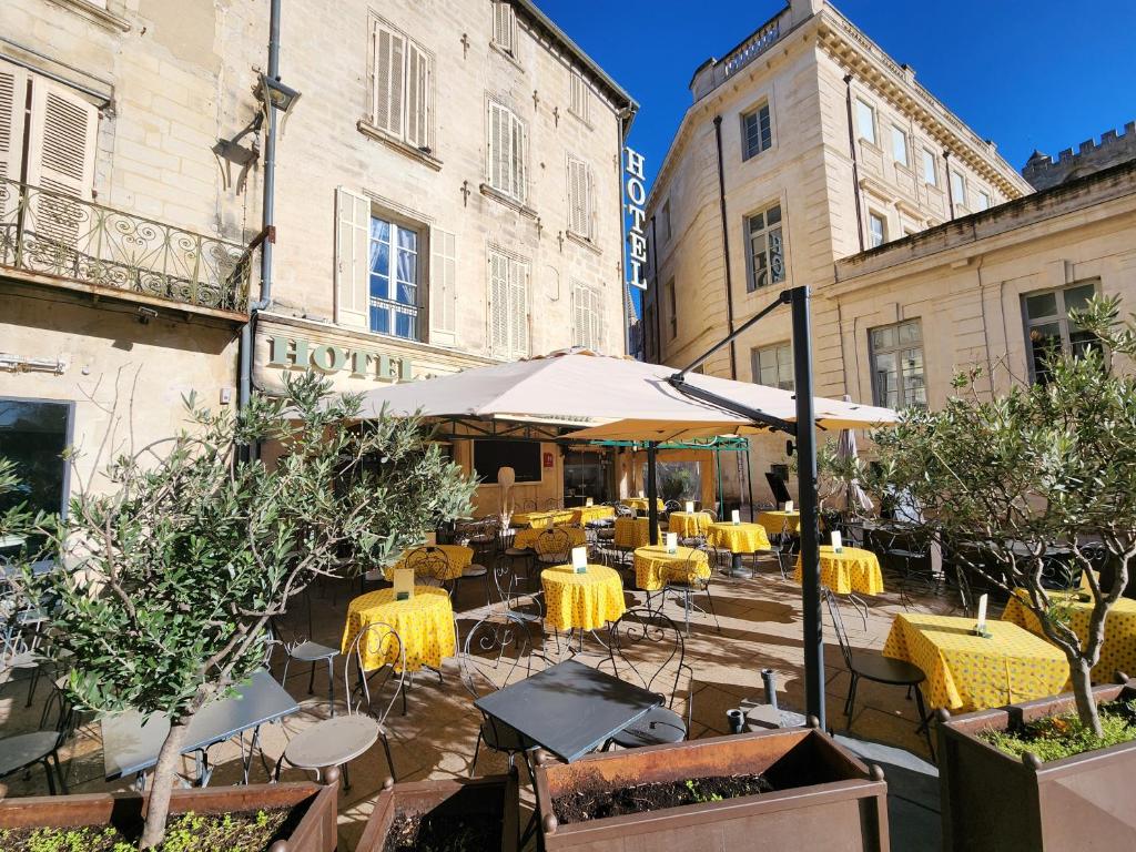 an outdoor cafe with yellow tables and chairs and buildings at Hôtel du Palais des Papes in Avignon
