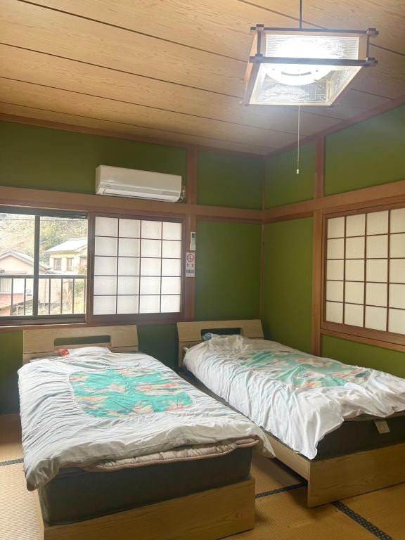 two beds in a room with green walls and windows at tsudoi in Tanabe