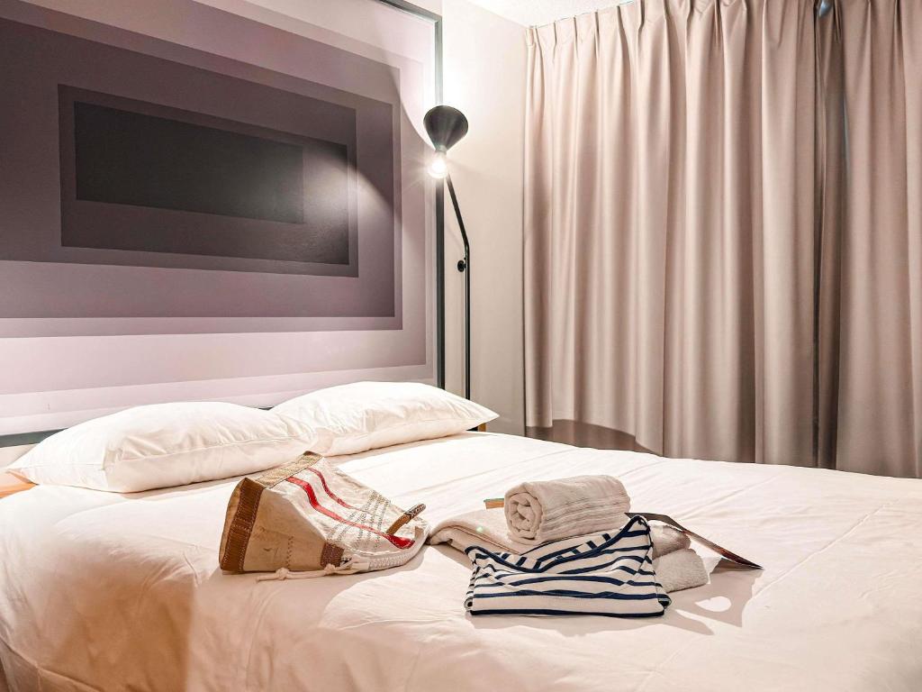 a white bed with clothes and a lamp on it at ibis Rennes Beaulieu in Cesson-Sévigné