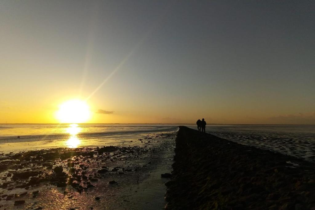 two people walking on the beach at sunset at Haus Weitwinkel in Sehestedt