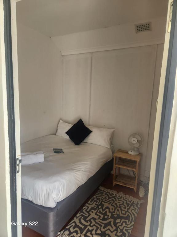 a small bedroom with a white bed with a black pillow at Forest Gate Backpackers in Plettenberg Bay