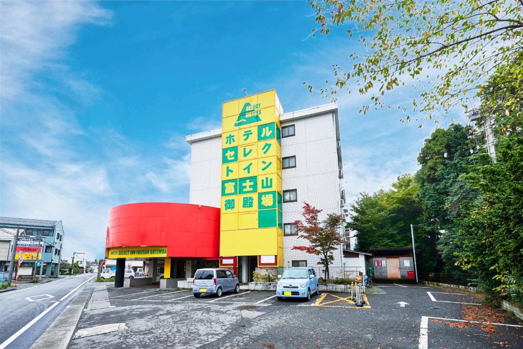 Select Inn Fujisan Gotemba في غوتيمبا: مبنى اصفر و ابيض و فيه سيارات متوقفة في موقف