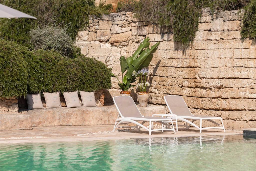two white chairs sitting next to a swimming pool at Cava Li Santi Residence a Santa Caterina in Nardò