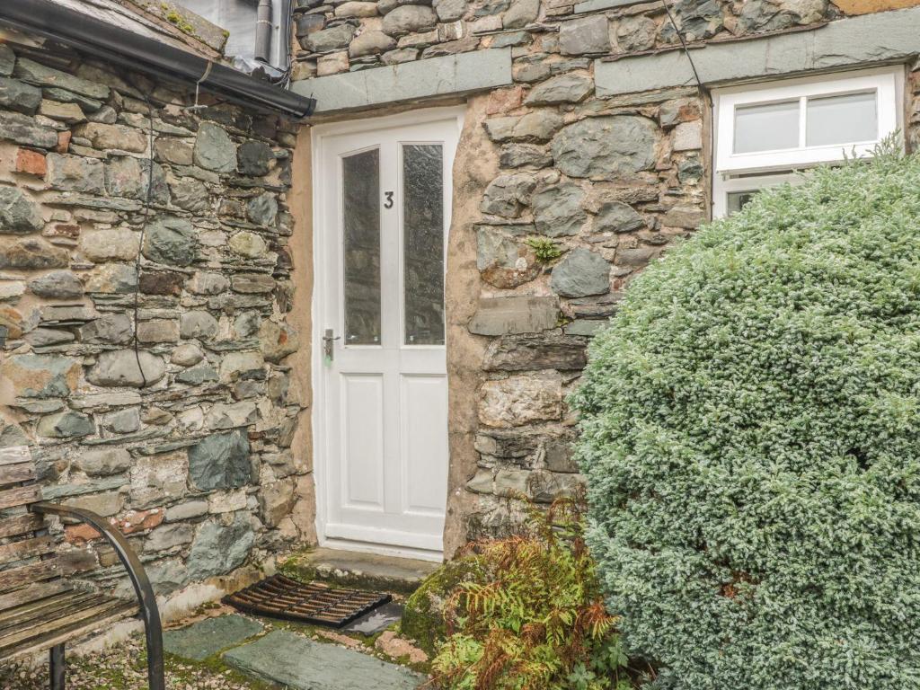 a stone house with a white door and a bush at Cottage 3 in Keswick