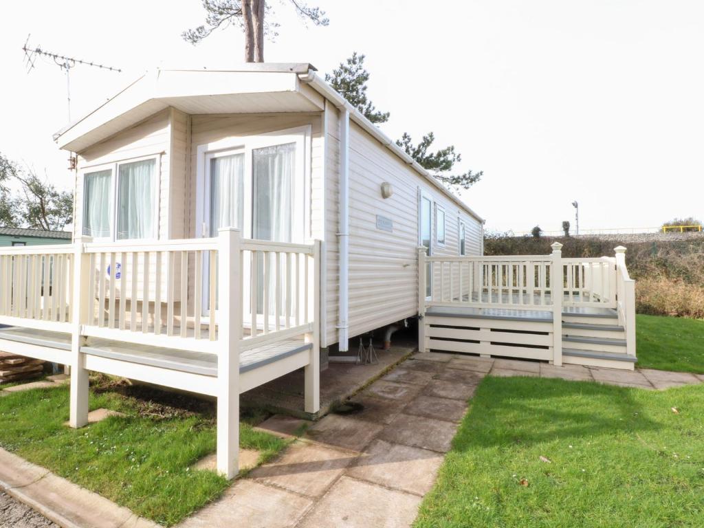 a white tiny house with a porch and a fence at Under Cliff Caravan in Ferryside