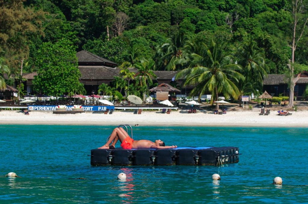 a man laying on anlatable raft in the water at a beach at Perhentian Island Resort in Perhentian Islands