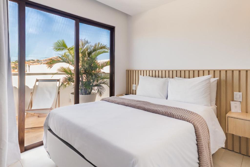a bedroom with a white bed and a large window at Onda Lofts in Búzios