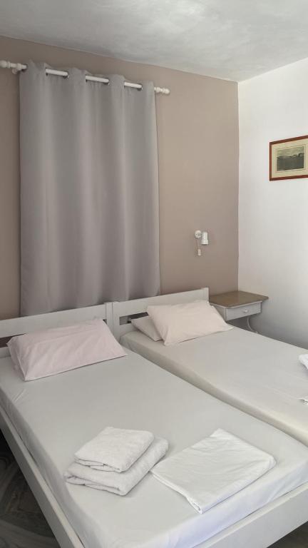 two beds in a room with white sheets and towels at Akrogiali Hotel in Agios Sostis