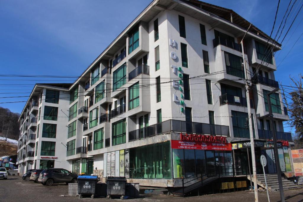 a white building with green windows on a street at Hotel Bobline 304 in Bakuriani