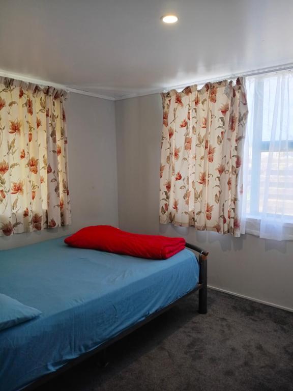 a bed with a red pillow in a room with curtains at Papamoa cheep holiday accommodations in Papamoa