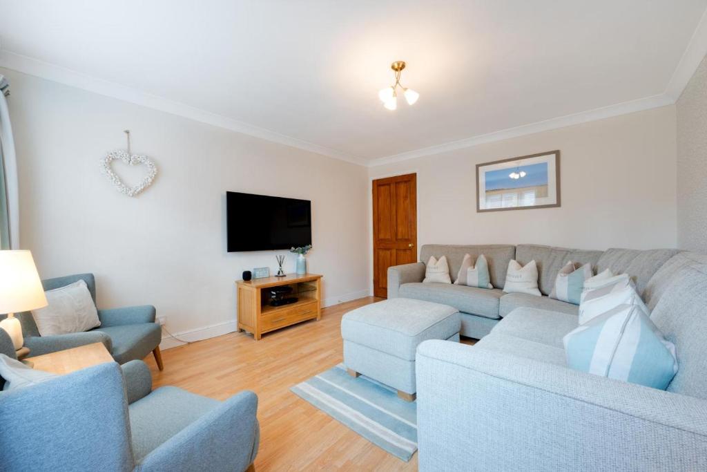 Living room with light grey sectional sofa, two blue armchairs, wooden TV stand, and wall-mounted flat screen TV
