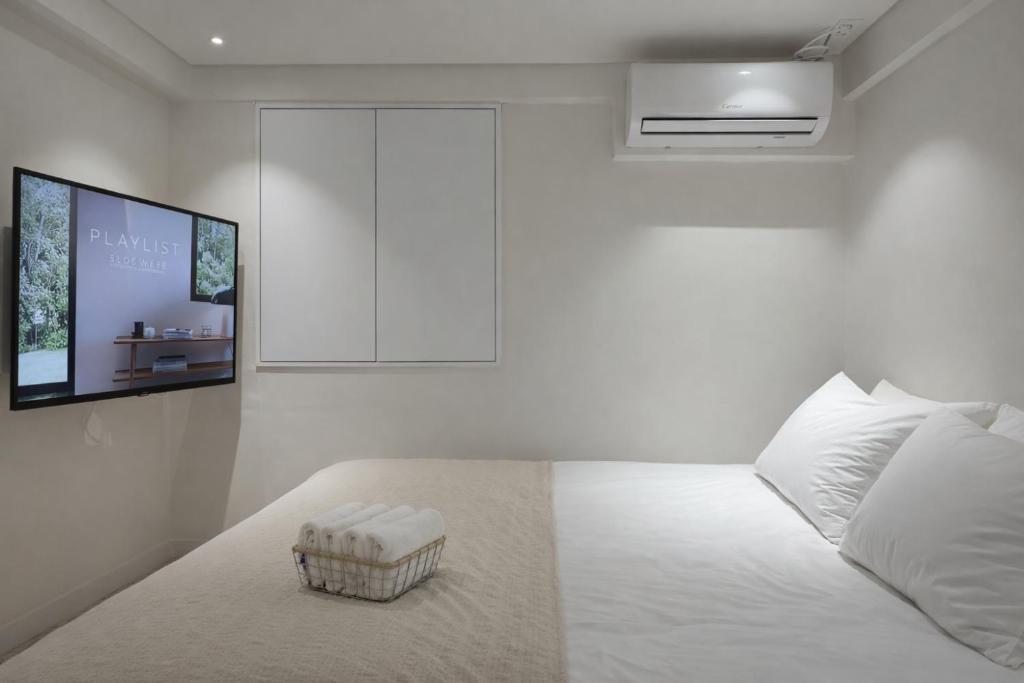 a white bedroom with a bed with a tv on the wall at Staymoment in Seoul