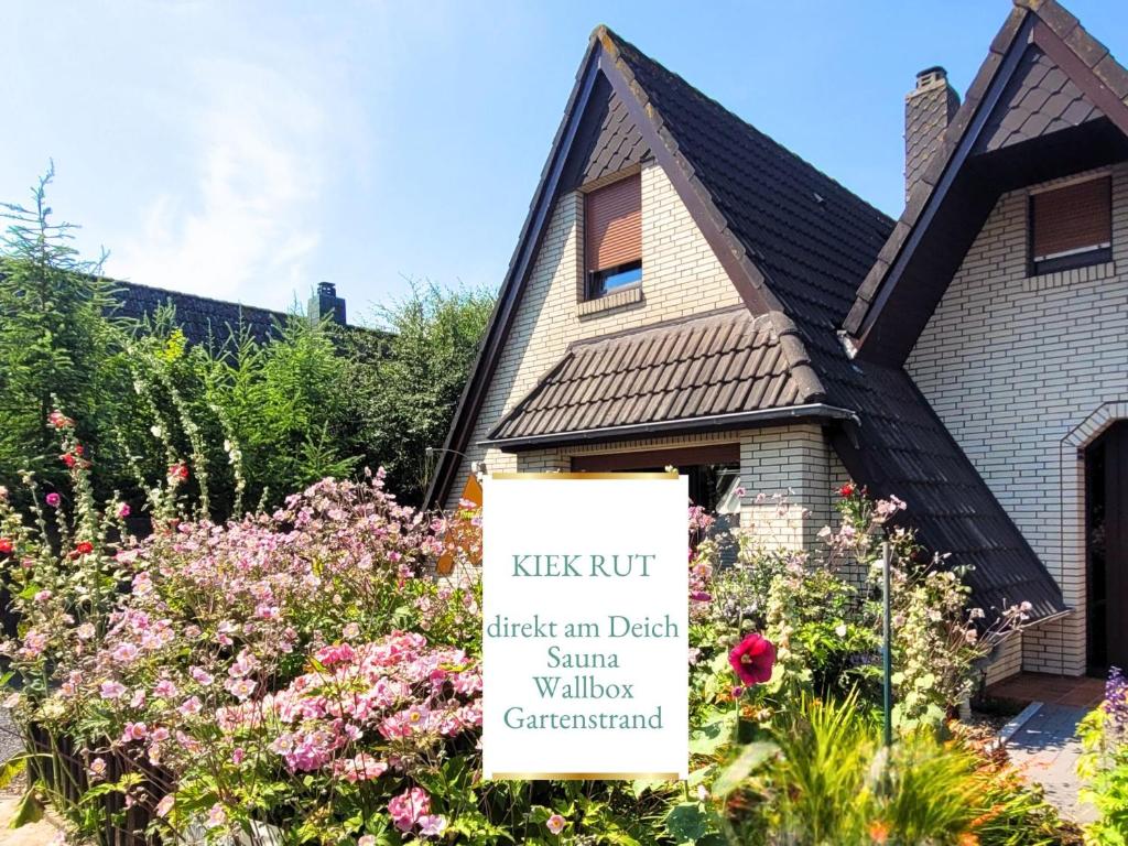 a sign in front of a house with flowers at Ferienwohnung KIEK RUT - Gartenstrand, Wallbox & Sauna, alles für die Familie, zusätzlicher Loft in Harlesiel in Wittmund