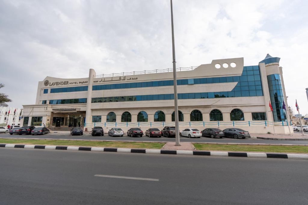 a large building with cars parked in a parking lot at Lavender Hotel Sharjah in Sharjah