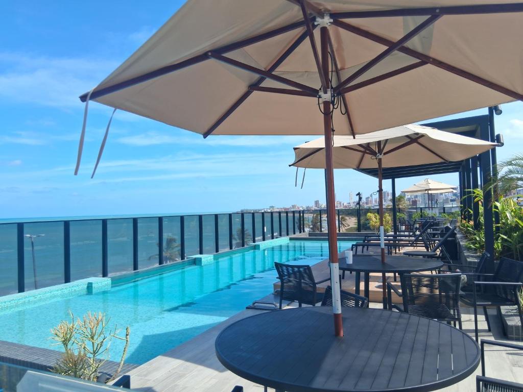 a pool with tables and umbrellas on a balcony at Flat Beach Haus a beira mar João pessoa in João Pessoa