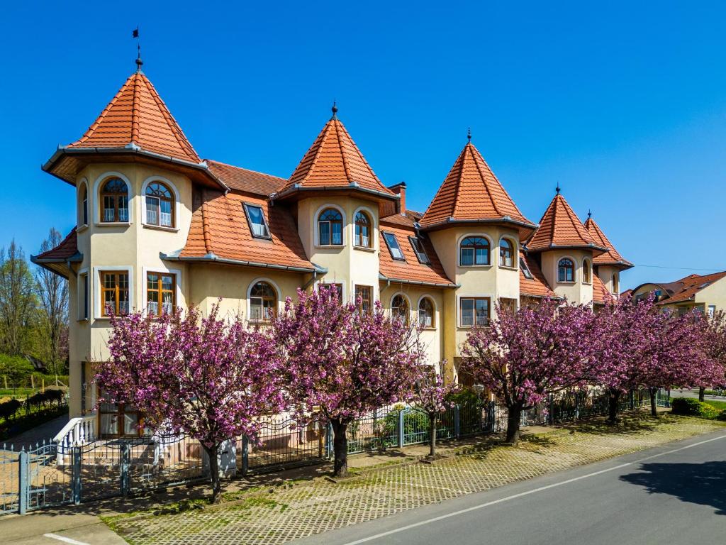 a large house with turrets and purple trees at Hajdú Kastély Hotel in Hajdúszoboszló