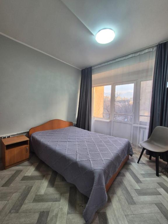 a bedroom with a bed and a window and a chair at Альтаир in Almaty